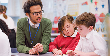 Photo d'un professeur assis à côté de deux écoliers regardant un cahier dans une classe