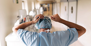 Photo d'un docteur de dos en blouse réajustant son masque dans un couloir d'hôpital