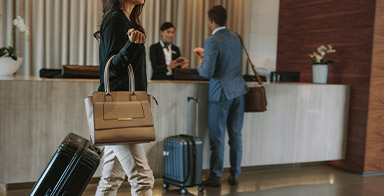 Photo d'un hall d'hôtel avec, au premier plan, une femme tirant son bagage et, en arrière-plan, un comptoir avec un homme en discussion avec le réceptionniste